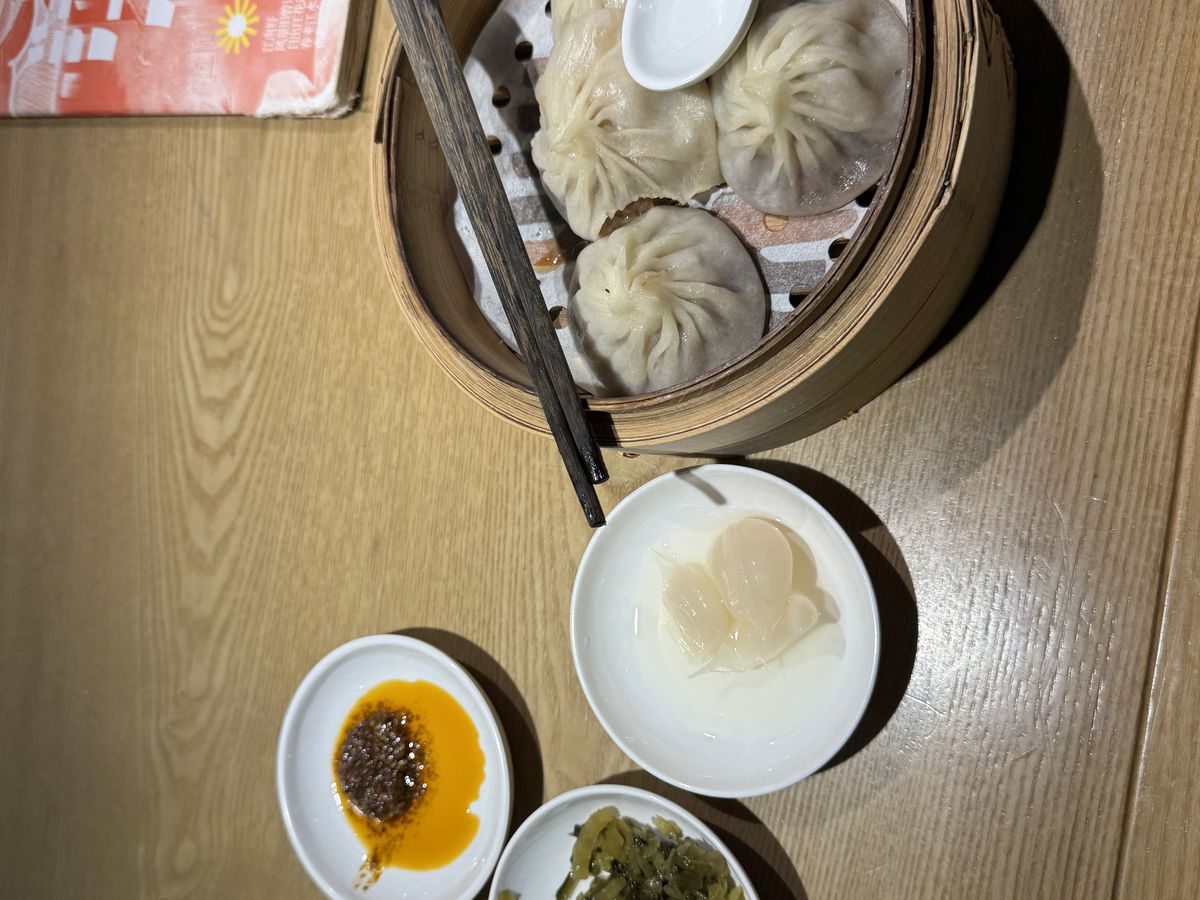 Jambosim Review: Is This Cheap Esim Worth It? (Honest Test) A bamboo steamer of xiaolongbao soup dumplings with chili oil and pickles on a restaurant table in beijing